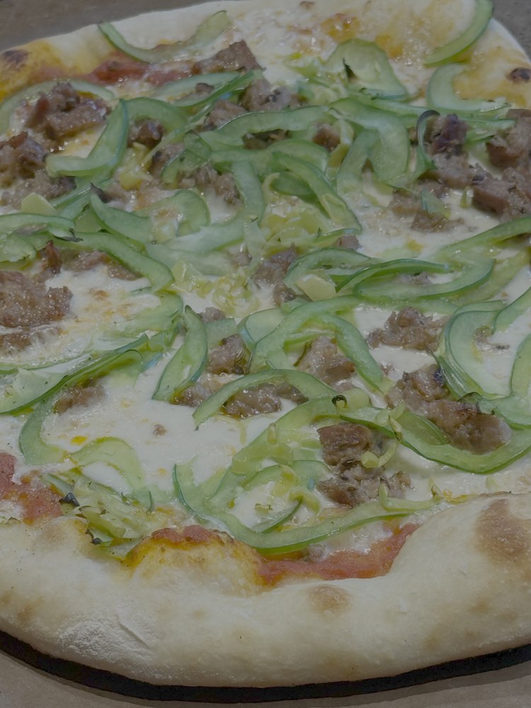 Wood-fired pizza with fresh basil, ground meat, and melted cheese